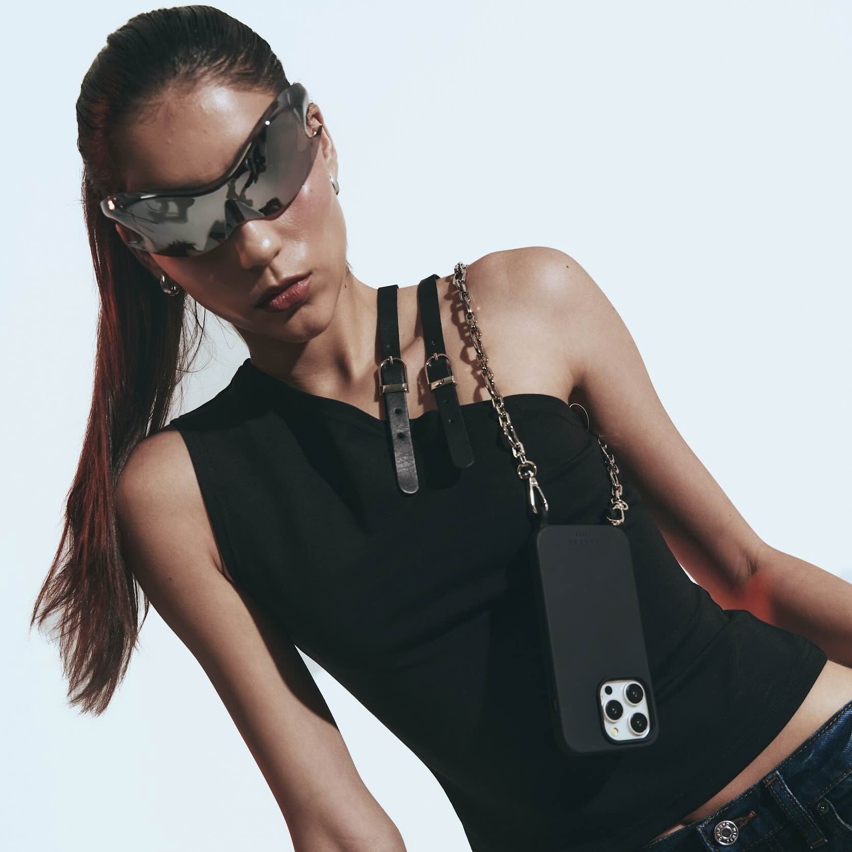 Woman wearing a black sleeveless top with a phone case attached, against a plain background