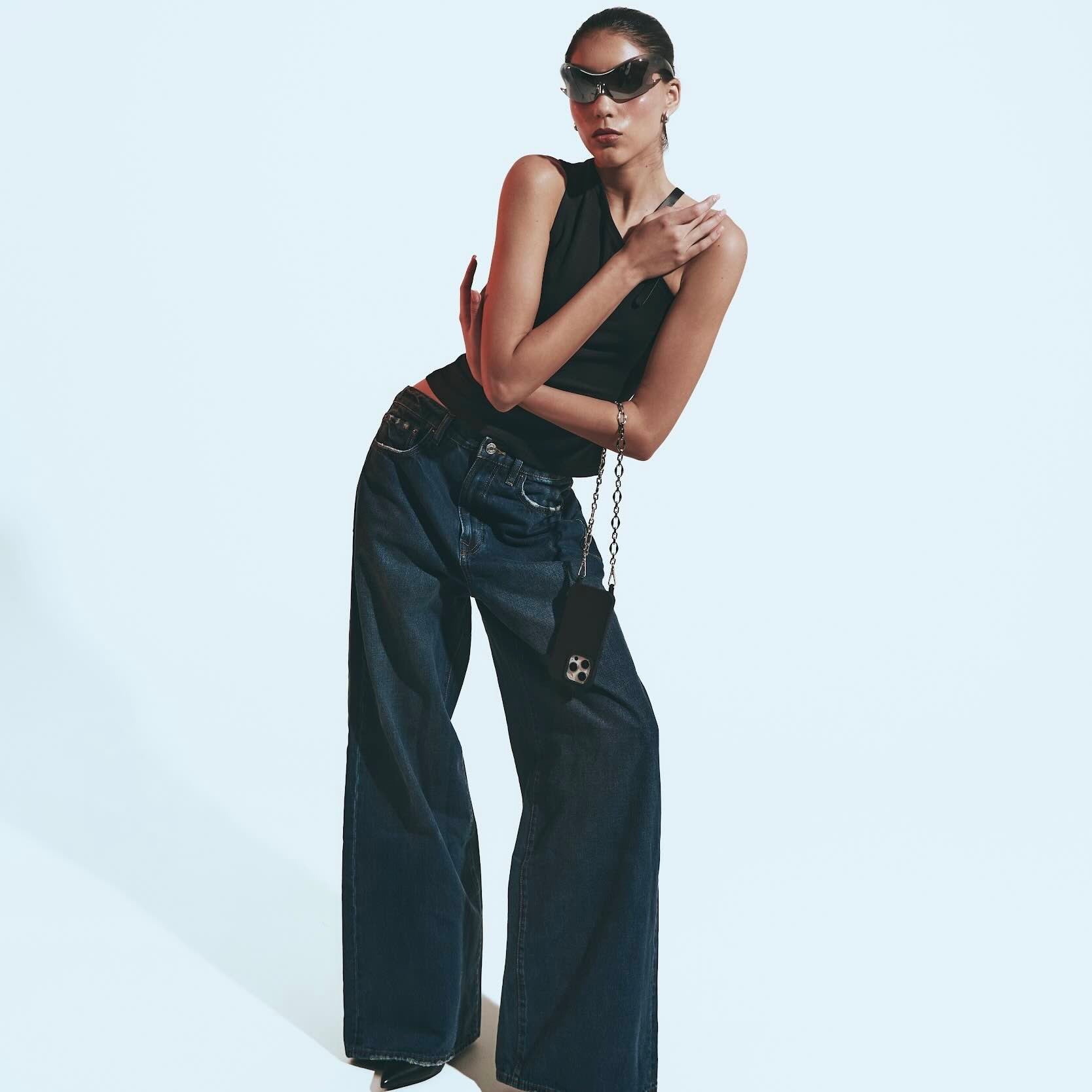 Woman wearing a black sleeveless top and dark blue jeans on a light gray background