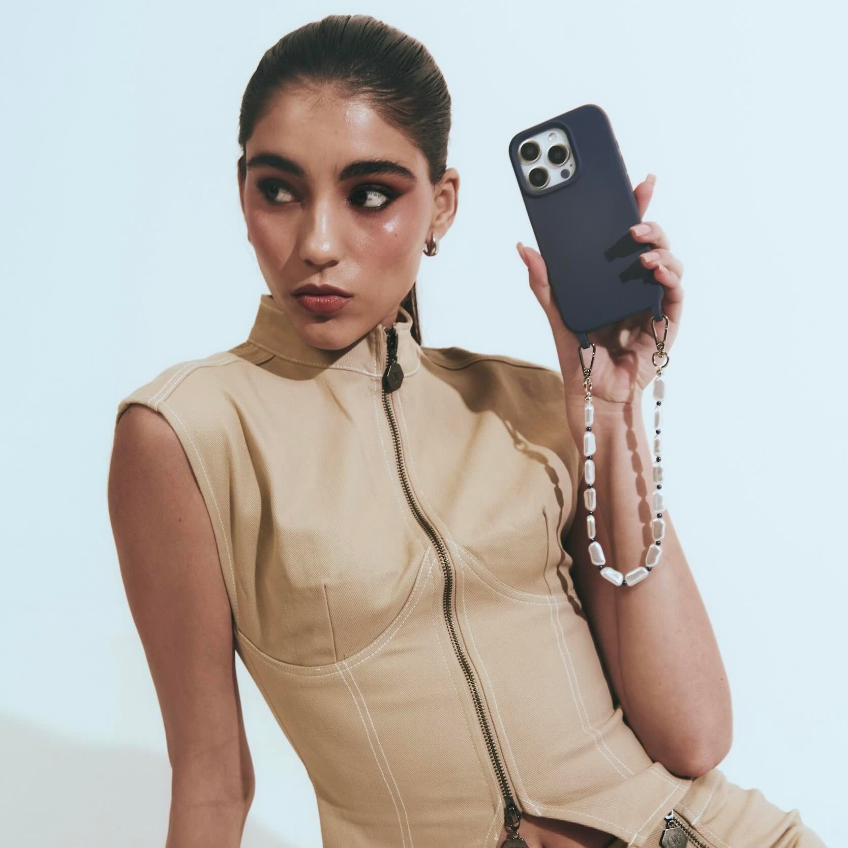 Woman in beige sleeveless top holding a phone with a white background