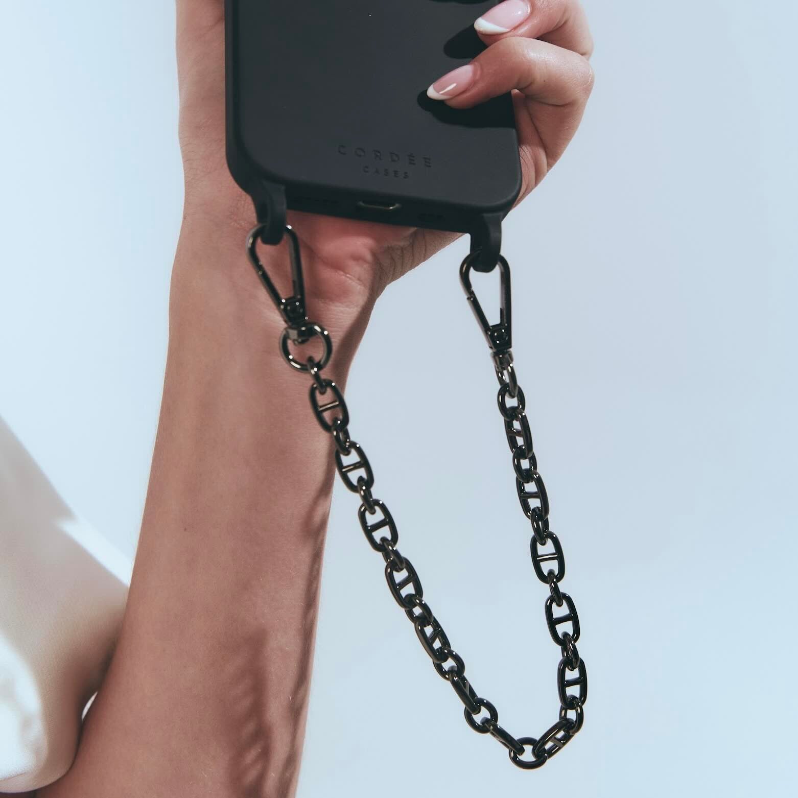Hand holding a black phone case with a chain strap against a light blue background