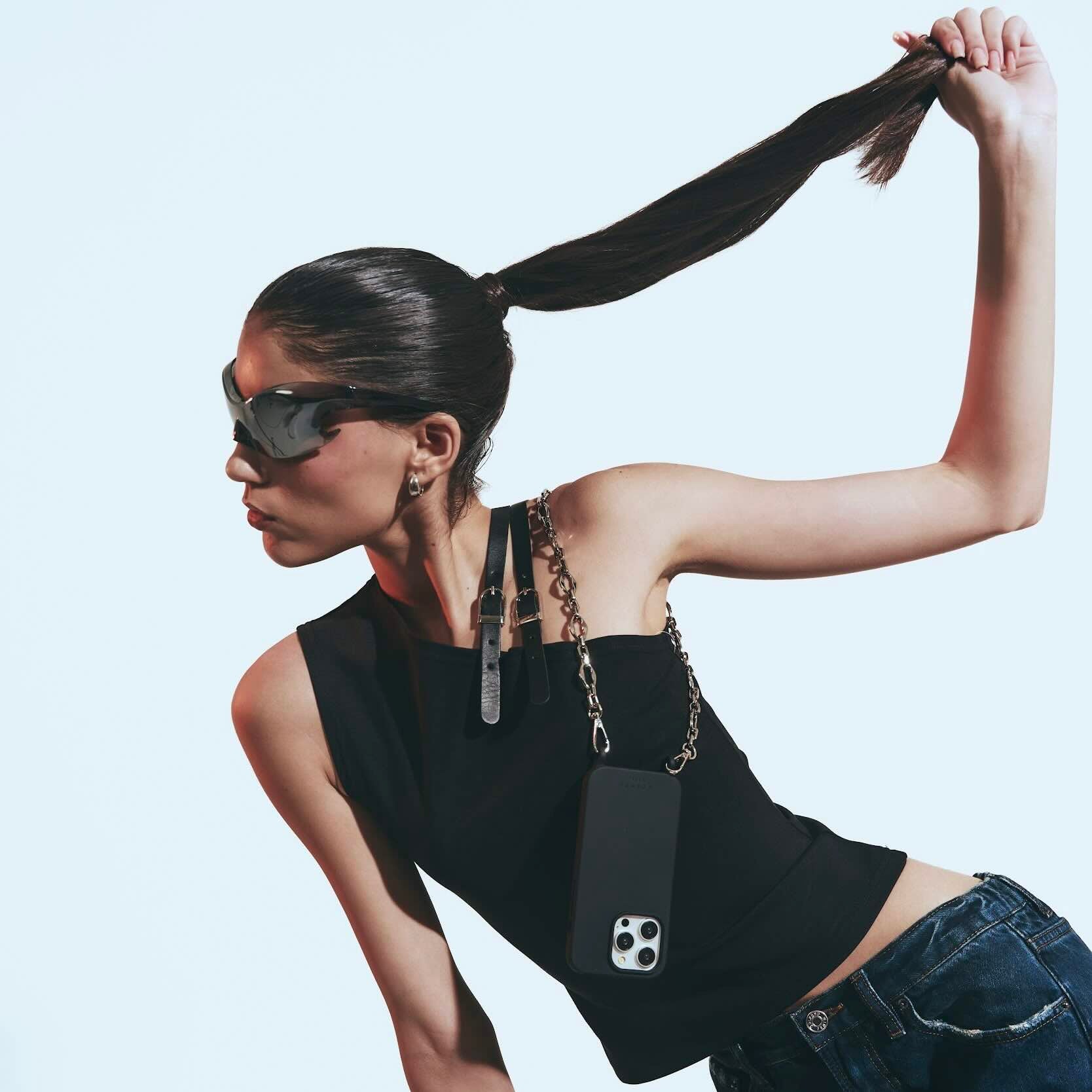 Woman with sunglasses and a black sleeveless top with a phone case, on a light gray background