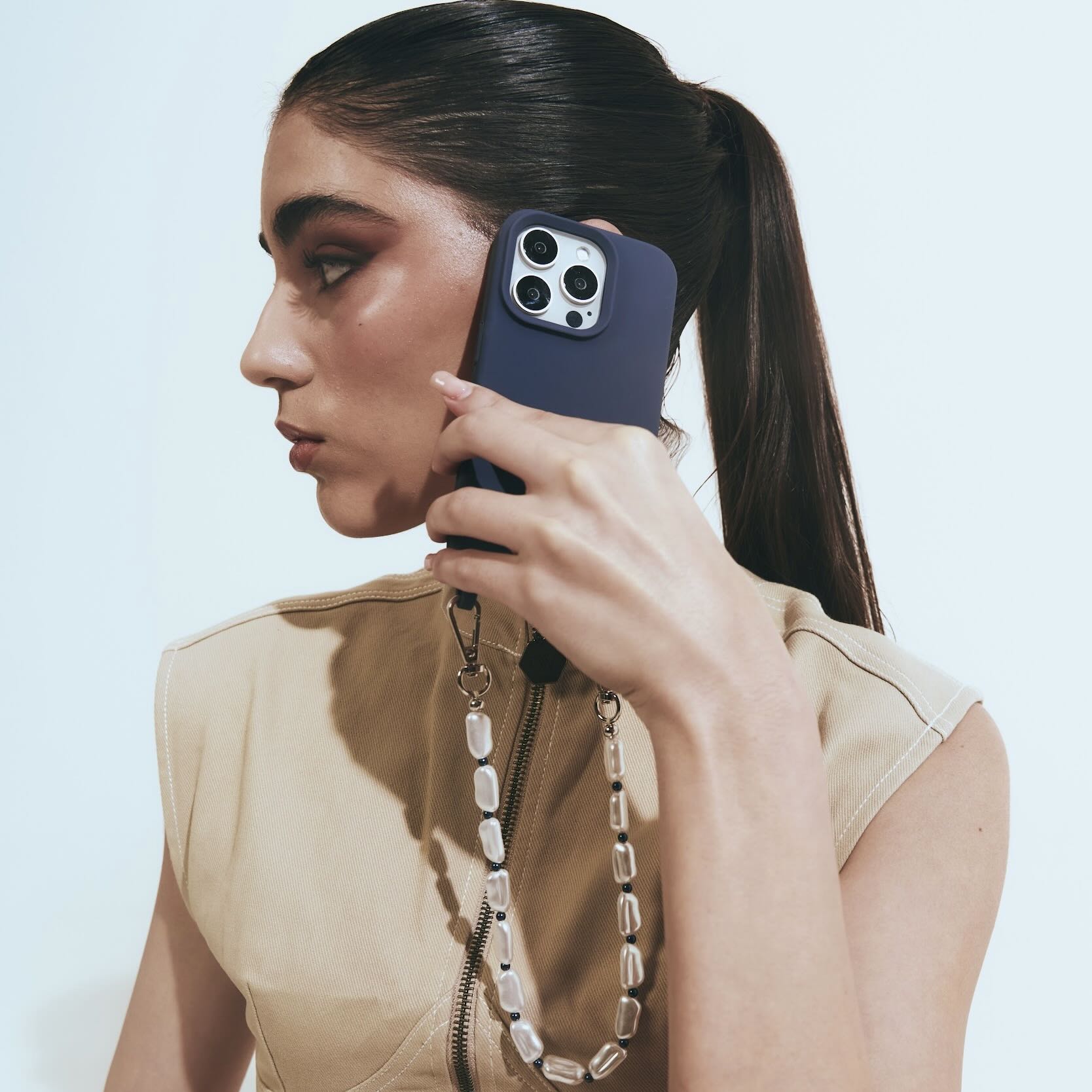 Woman holding a phone with a blue case and phone wrist strap against a light background